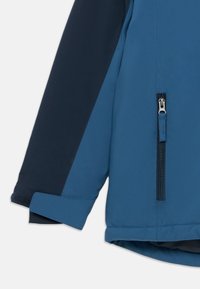 Casaco impermeável azul e marinho com bolso lateral com zíper, textura suave e um corte descontraído, com um acabamento em punho suave e contrastante.