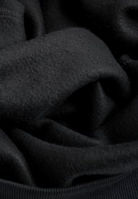 Zwart fleece stof, zachte textuur, met een licht gerimpeld uiterlijk. Heeft een ribbelrand aan de onderkant, wat het gezellige ontwerp benadrukt.