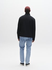 Svart glidelåsjakke, blå jeans og svarte joggesko. Bakfra vises enkel design, ensfargede plagg og en burgunder caps. Ingen mønstre eller detaljer.