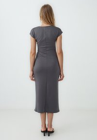 Abito midi grigio con maniche a cappuccio, silhouette aderente, dettagli sulle cuciture laterali e una sottile spacco posteriore. Realizzato in tessuto morbido e elastico.