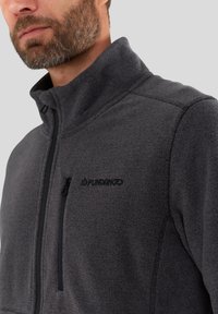 Grijze fleecejas met hoge kraag, ritszak op de borst en een logo aan de linkerkant. Heeft een gestructureerde stof en subtiele naaddetails.