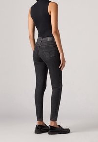 Černé džíny skinny z denimu s vysokým pasem, vybavené dvěma zadními kapsami a koženou značkou s logem na pásku. Hladká textura, přiléhavý střih.