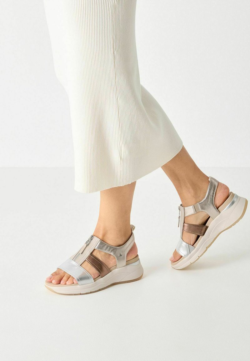 Sandali in bronzo e argento con chiusura a zip, open toe e più cinturini in un design a strati. Suola bianca spessa con accenti testurizzati.