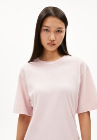 Helles rosa Oversize-T-Shirt aus weichem Baumwollstoff mit einem Rundhalsausschnitt und kurzen Ärmeln in lässiger Passform. Sanfte Textur und minimale Details.