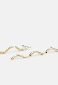 Guldtonade metallörhängen har en vågig design med släta, flödande former. Varje del har en stiftfäste för säker bärning.