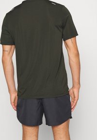 Camiseta atlética de manga corta en verde oliva, confeccionada con tejido ligero, presenta un cuello redondeado y detalles reflectantes en los hombros.