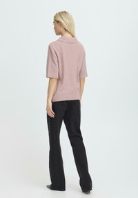 Pull en mélange de laine rose clair à manches courtes avec un col. Porté avec un jean noir évasé, mettant en valeur une coupe décontractée.
