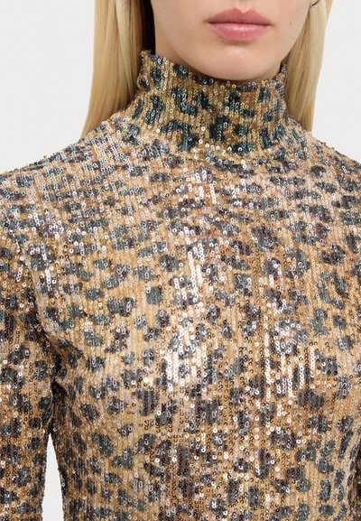 Zelts zeltītā turtlenecka augšdaļa ar leopardu rakstu un melniem un ziliem akcents. Gluda tekstūra un pieguļoša forma.