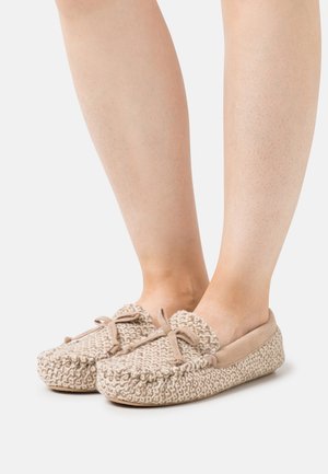Knit beige slippers with a soft cream lining, rounded toe, and bow detail on the front. Textured woven fabric and flat sole.