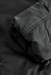 Schwarzer, gepolsterter Jackenärmel mit sichtbarer Steppung und Naht, zeigt Stofftextur und Isolationsdetails.