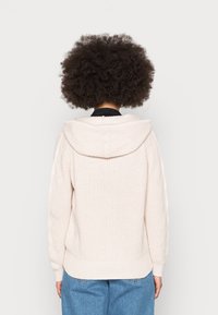Różowy dzianinowy hoodie o prążkowanej fakturze, z oversize'owym kapturem i rękawami w splot warkocza. Tył ma lekko skrócony krój.