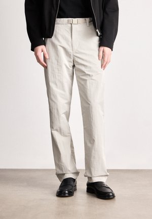 Svetlosivé textúrované nohavice so strihom rovného nohu a smotanovým opaskom. V kombinácii s čiernymi mokasínami, umiestnené na neutrálnom pozadí.