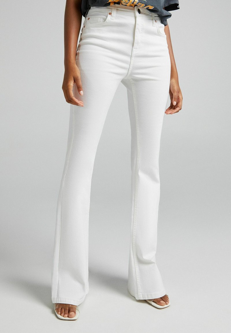 Jean flare blanc en tissu mélangé coton, avec une taille haute, des détails de couture subtils et une surface lisse et texturée.