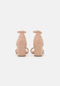 Nude block-heeled sandals with ankle straps. Smooth leather material, square-toe design, and gold-tone accents on the heel.