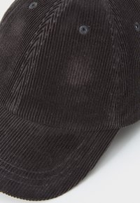 Black corduroy cap with vertical ridges, rounded crown, and curved brim. Features ventilation holes and textured fabric for a tactile feel.