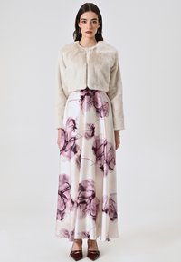 Veste en fausse fourrure courte crème sur une jupe maxi en satin ornée de motifs floraux violets. Des chaussures à talons hauts bordeaux viennent compléter le look.