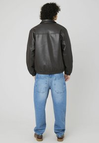 Veste bomber en cuir marron avec un col, taille élastique et jeans en denim bleu à coupe lâche, vu de dos.