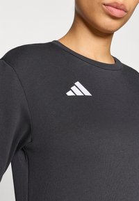 Μαύρο αθλητικό πουκάμισο με στρογγυλή λαιμόκοψη και λευκό λογότυπο Adidas στο πάνω αριστερό μέρος. Κατασκευασμένο από απαλό ύφασμ α με εφαρμοστή σχεδίαση.