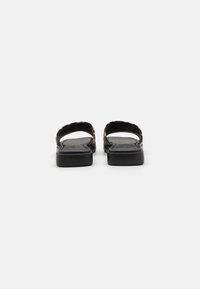 Black sandals with a low heel, featuring an open back and crossover straps with a tortoiseshell pattern on the edges. Flat sole design.