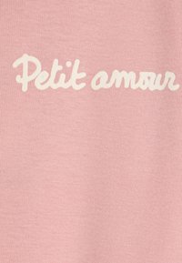 Ružová látka so textom "Petit amour" v bielom, písaným štýlom. Textúra je hladká s jemným ryhovaným povrchom.