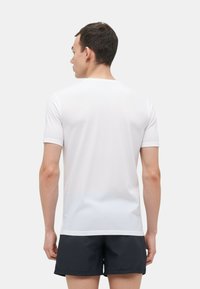 T-shirt bianco a maniche corte con collo rotondo, tessuto liscio e cuciture a contrasto sulle maniche. Indossato con pantaloni corti scuri.