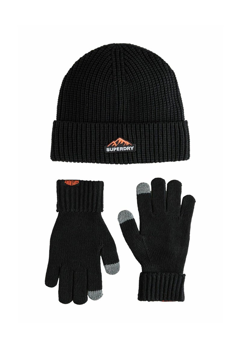 Zwarte gebreide beanie met ribbeltextuur en oranje berglogo; zwarte handschoenen met ribbelmanchetten en grijze vingertopdetails.