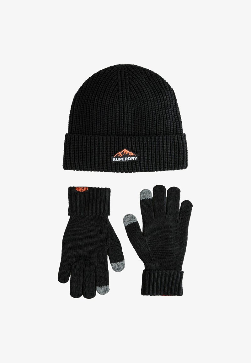 Zwarte gebreide beanie met ribbeltextuur en oranje berglogo; zwarte handschoenen met ribbelmanchetten en grijze vingertopdetails.