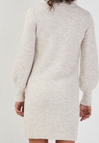 Robe en maille beige clair avec une texture douce, manches longues ballon et ourlet côtelé. Le modèle présente un motif subtil sur toute la surface.