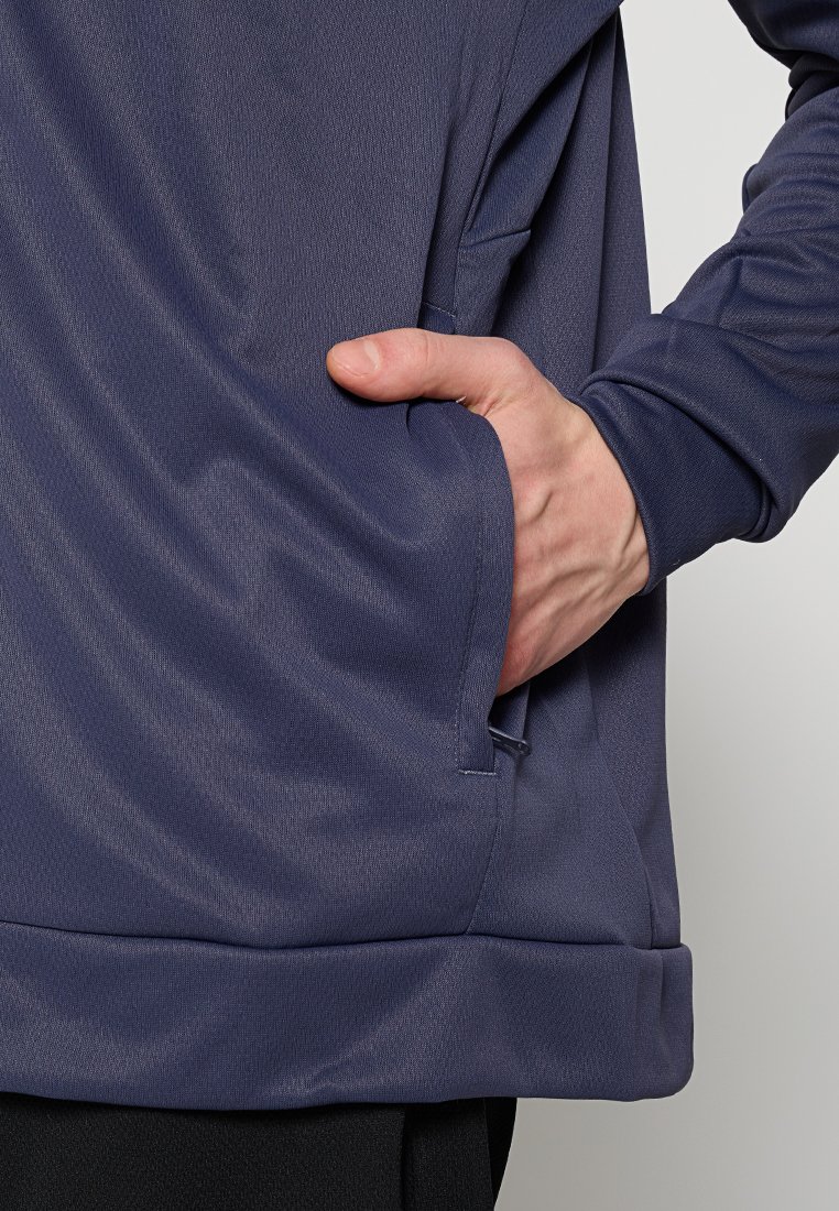 Pull-over de sport navy avec une poche latérale, texture lisse et coupe décontractée avec un ourlet côtelé. Main visible dans la poche.