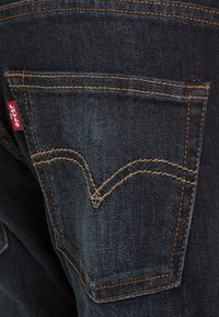 Tummansiniset farkut, joissa on takatasku, jossa on erottuva kaareva ommelkuvio ja vasemmalla puolella punainen Levi's-tunnus.