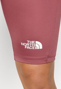 Bordowe szorty sportowe o gładkiej, elastycznej teksturze. Na dolnej lewej nogawce znajduje się biały logo "The North Face".