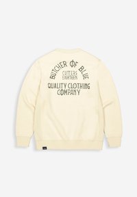Creme kleurige sweatshirt met een gestructureerde afwerking, met op de achterkant donkergroene tekst: "BUTCHER OF BLUE CUTTERS EIGHTEEN QUALITY CLOTHING COMPANY."