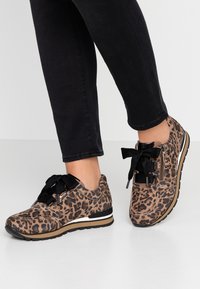 Baskets à imprimé léopard avec des lacets noirs, un design profil bas, un tissu texturé et une semelle blanche et noire en accent.