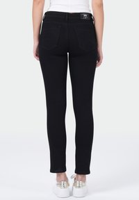 Zwarte skinny jeans met een gladde textuur, twee achterzakken en een subtiele logo-label bij de tailleband. Heeft een slim fit en een tapered leg.