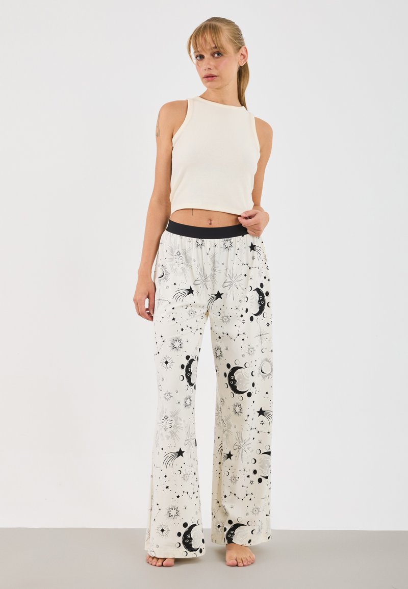 Valkoinen ribbipintainen crop-top yhdistettynä leveälahkeisiin housuihin, joissa on mustavalkea taivaankappaleprintti, joka sisältää tähtiä, kuita ja auringon kuvioita.