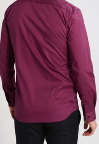 Chemise à manches longues bordeaux avec une texture lisse, des poignets à boutons et un empiècement dos droit pour une coupe ajustée.