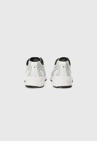 Baskets blanches de sport avec une tige en maille et des accents noirs, dotées d'une semelle rembourrée, d'un logo visible et d'un talon structuré pour le soutien.