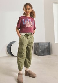 Mörkröd kortärmad t-shirt med texten "MICHIGAN 82", olivgröna cargobyxor, bruna slip-on skor och beige strumpor. En enkel och avslappnad outfit.