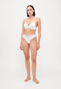 Ensemble de lingerie blanche comprenant un soutien-gorge plongeant avec des bretelles fines et un slip taille haute assorti, arborant une ceinture avec le logo gris "HUGO".