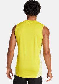 Maglietta atletica senza maniche in tessuto giallo brillante con una texture liscia, caratterizzata da pannelli laterali di un giallo chiaro a contrasto e un collo a giro.