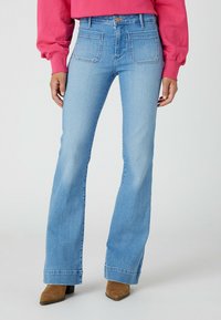 Jeans svasati di colore azzurro chiaro con vita alta, cinque tasche e cuciture a contrasto, abbinati a stivaletti a punta marroni.