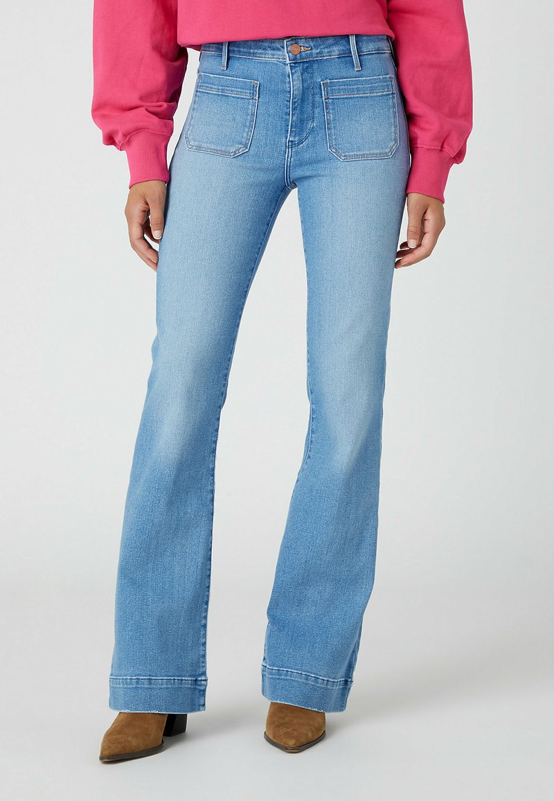 Jeans svasati di colore azzurro chiaro con vita alta, cinque tasche e cuciture a contrasto, abbinati a stivaletti a punta marroni.