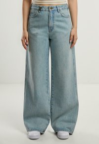 Jeans evazați de culoare albastru deschis, realizate din denim. Design cu talie înaltă, cu buzunare frontale, cusături vizibile și o siluetă dreaptă.