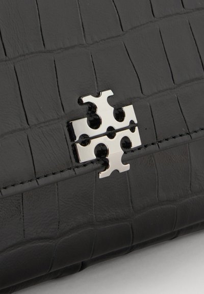 Surface en cuir noir texturé avec un fermoir brillant en forme de pièce de puzzle argentée centré sur une couture cousue.