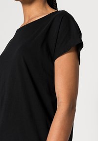 T-shirt nera in cotone con vestibilità ampia, maniche corte e scollatura larga. Texture liscia con colore uniforme, senza motivi visibili.