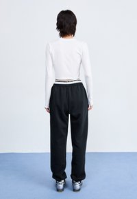 Top corto blanco de manga larga con escote redondo, combinado con pantalones de chándal negros y holgados y zapatillas grises con detalles negros.