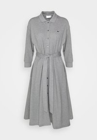 Robe mi-longue gris clair à manches longues, boutonnée avec col, ceinture en tissu nouée à la taille et petit logo brodé sur la poitrine.