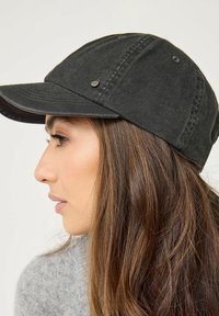 Svart bomullscap med en böjd skärm och nitar, med en slät yta. Har en liten varumärkesdetalj nära framsidan.