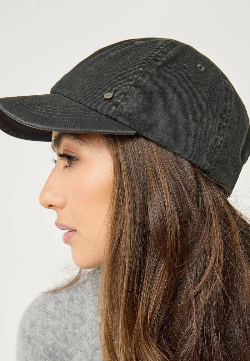 Svart bomullscap med en böjd skärm och nitar, med en slät yta. Har en liten varumärkesdetalj nära framsidan.