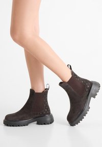 Brown suede ankle boots with textured knit panel, chunky rubber sole, and pull tab. Features subtle branding on sides.